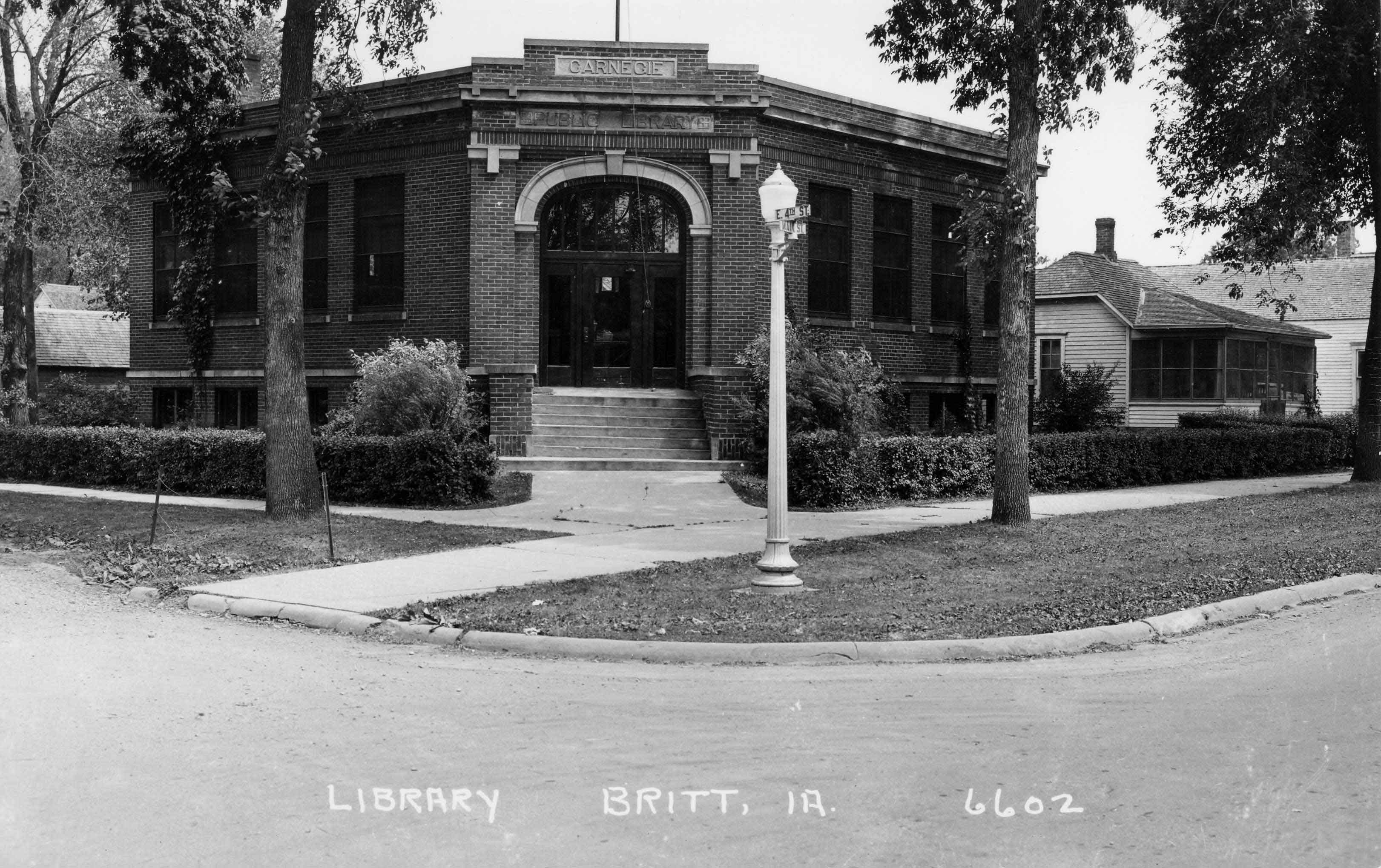 Black and white photograph depicting the exterior front of the Britt Public Library. Text reads "Library Britt, IA 6602." Source: unknown.