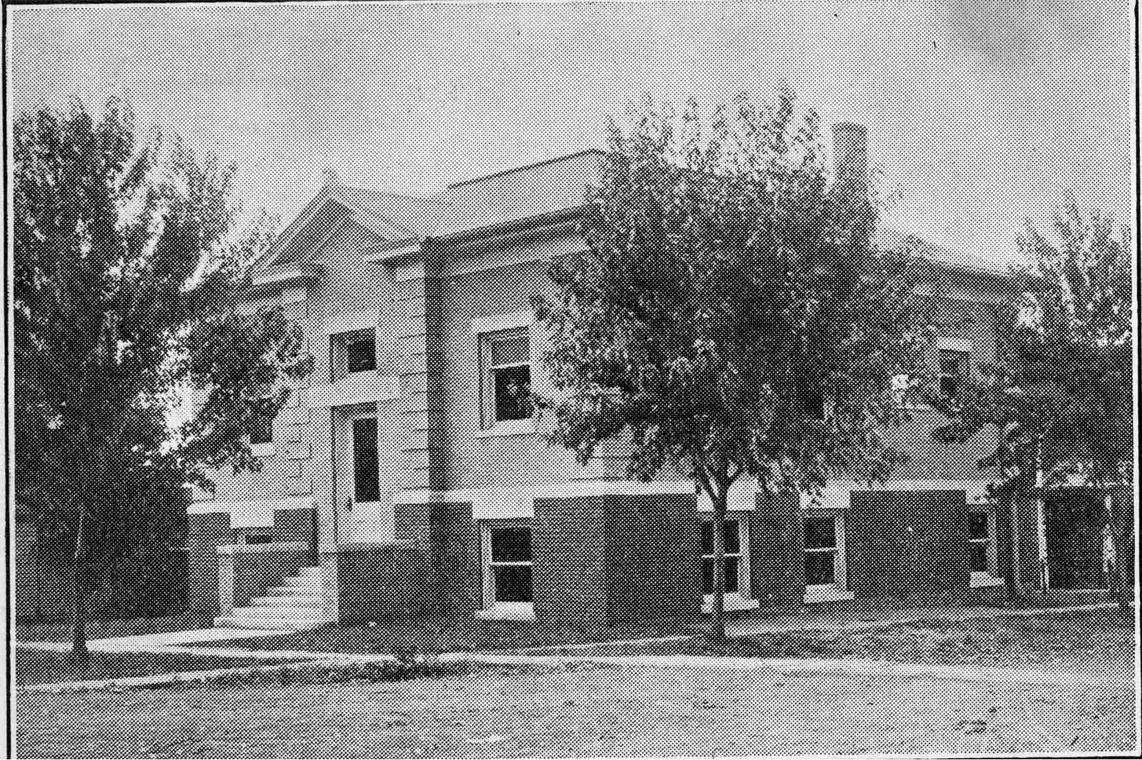 Black and white image depicting the front exterior of the Leon Public Library. Trees partially blocking the view of the building. 