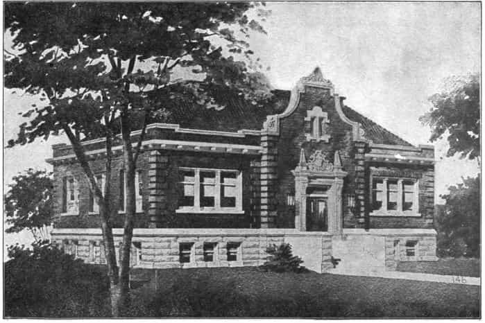 Black and white image showing the exterior of the of the Vinton Public Library; tree is partially blocking left side view. 
