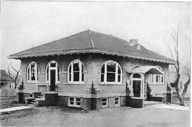 Black and white image showing the front and side exterior of the Woodbine Public Library. Image taken from the 5th Report of the Iowa Library Commission, coverage 1908-1910. (Published in 1909), unnumbered page between 32-33. 