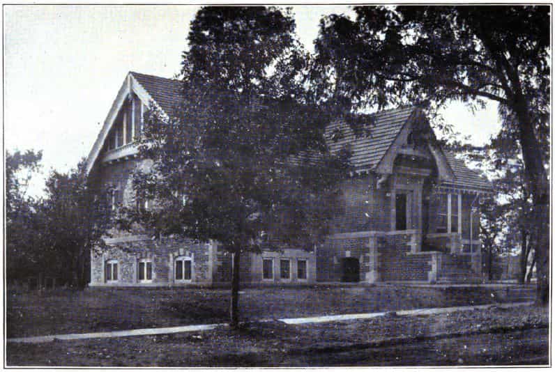 Black and white image showing the exterior of the Bloomfield Public Library. Trees are blocking most of the view of the building. Taken from the 7th Report of the Iowa Library Commission, coverage 1912-1914. (Published in 1914), opposite dedication page.