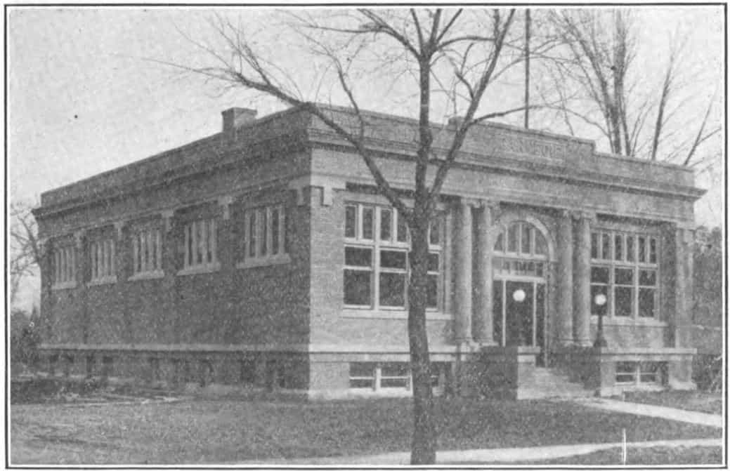 Black and white image showing the front and side exterior of the Clear Lake Public Library. Tree partially blocking view of the building. Taken from the 9th Report of the Iowa Library Commission, coverage 1916-1918. (Published in 1918), page 12.