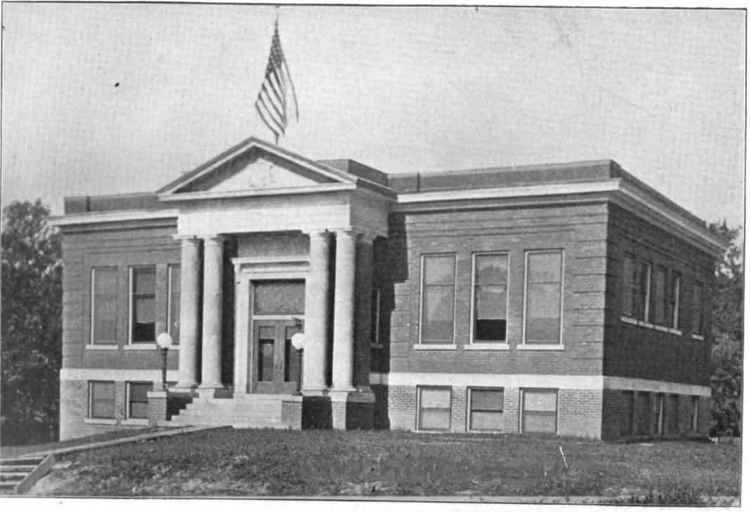 Black and white image showing the front exterior of the Missouri Valley Public Library. An American flag is also visible above the building. Taken from the 6th Report of the Iowa Library Commission, coverage 1910-1912. (Published in 1913), unnumbered page between pages 16-17.