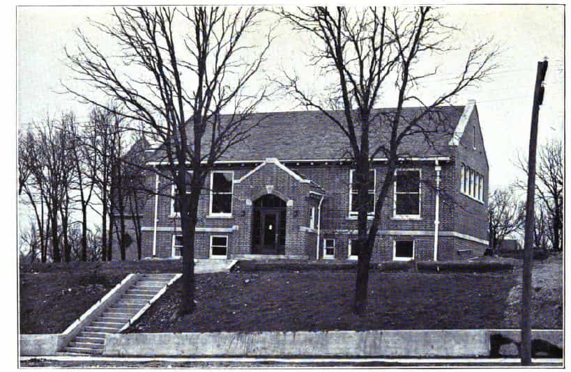 Black and white image showing the front exterior of the Sac City Public Library. Two trees are partially blocking the view of the building. Taken from the 7th Report of the Iowa Library Commission, coverage 1912-1914. (Published in 1914), opposite page 21.