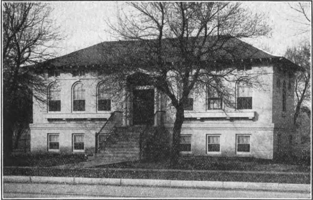 Black and white image of the Leeds Branch of the Sioux City Public Library. Tree partially blocking view of building. Taken from the 9th Report of the Iowa Library Commission, coverage 1916-1918. (Published in 1918), page 6.