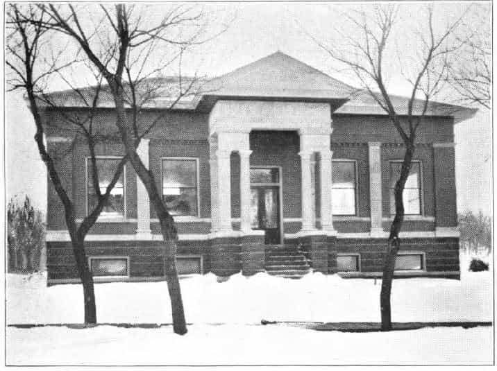 Black and white image depicting the front exterior of the Odebolt Public Library. Trees partially block the view of the building. 