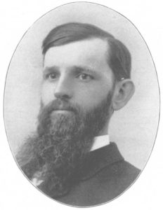 A bust photograph of Joseph Rich. He is wearing a suit with his hair slicked down and has a long beard.