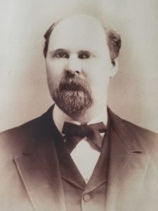 A picture of Mr O N Wagley a member of the Library Board in Newton Iowa. He is wearing a suit and coat, and is looking away from the camera slightly. His head is balding on the top and he has a long goatee style beard.