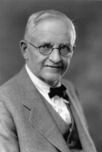 A black and white bust shot of an older Bohumil Shimek. He is wearing a suit and bowtie, has short white hair and mustache, and round glasses.