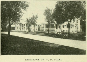 A black and white photo of W. P. Coast's residence. It depicts two large multi storage white houses with large columns and porches. There is also a black car parked in front of one house.